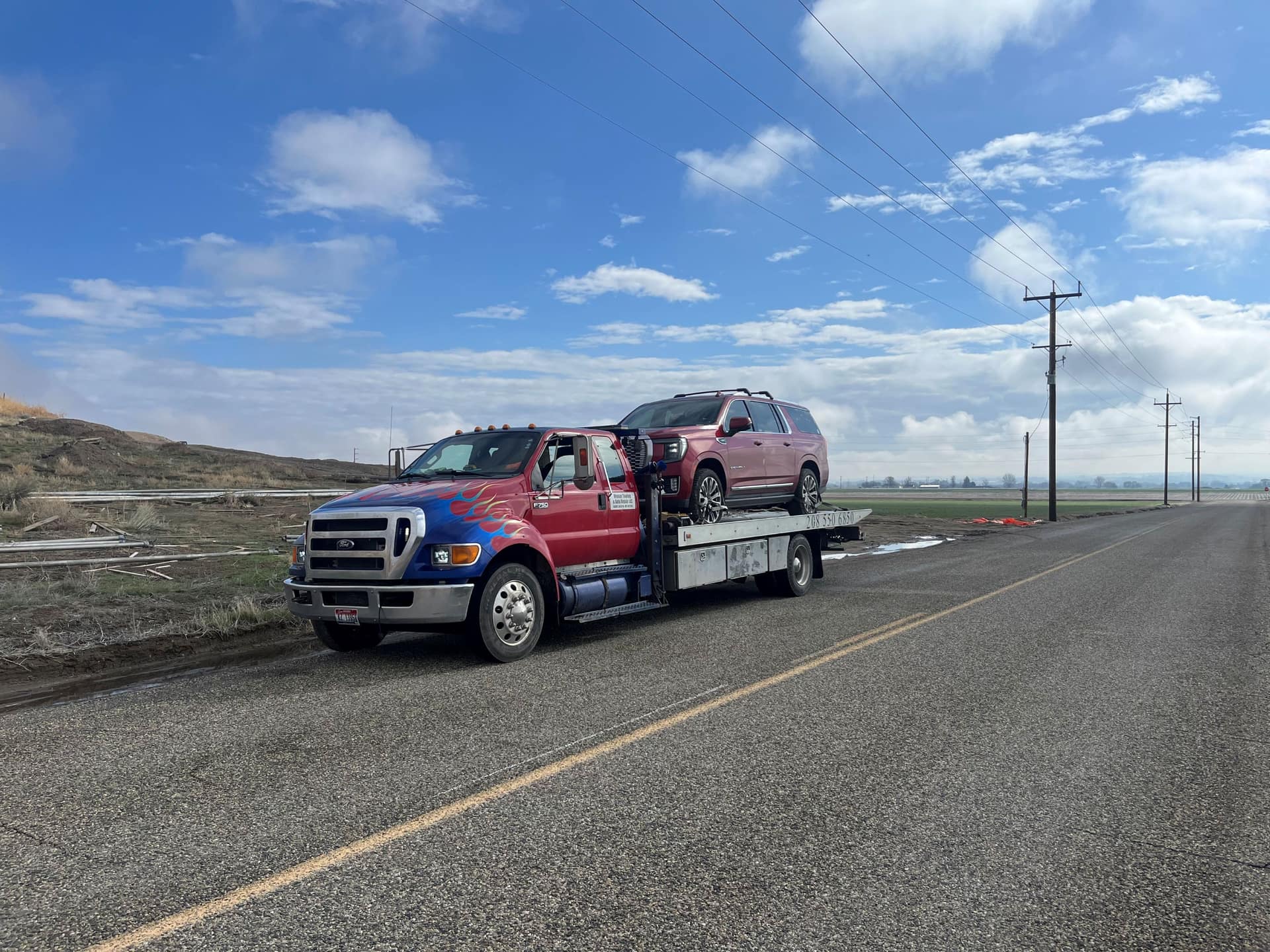 Weiser Towing flatbed carrying an SUV along a rural two-lane road through irrigated farm country
